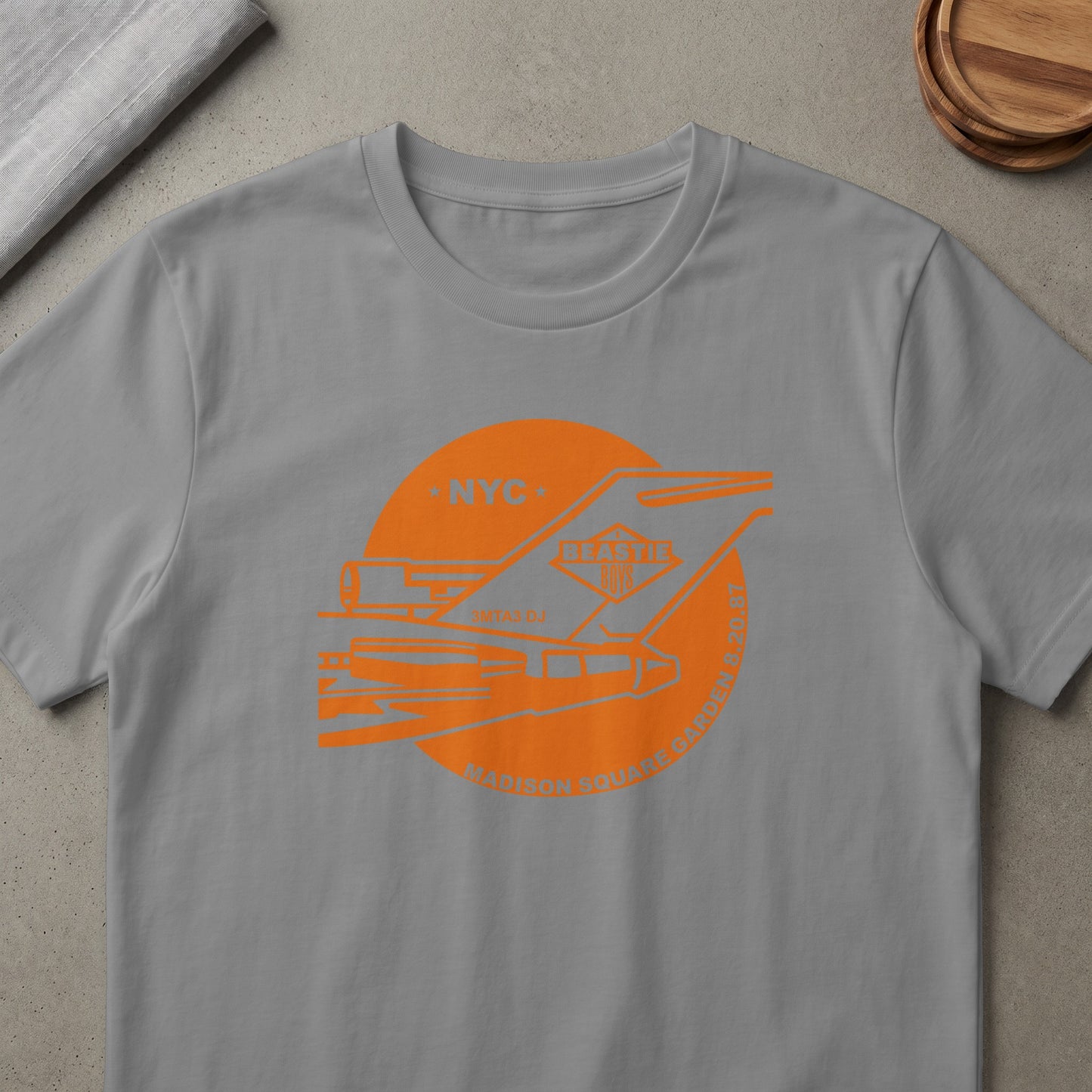 Grey t-shirt with orange graphic: NYC, Beastie Boys, 3MTAS DJ, Madison Square Garden 8.20.87.